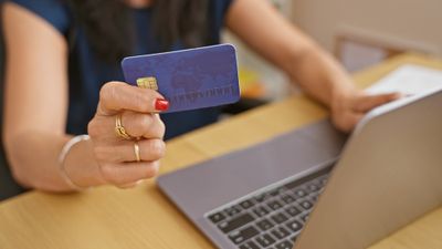 A woman holding a credit card in front of a laptop adding more items to her online shopping cart