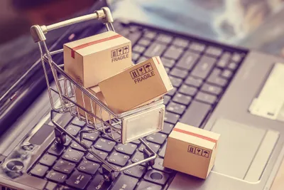 Tiny shopping cart filled with boxes sitting on top of a laptop keyboard to imply upselling and cross-selling